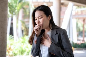 Picture of a woman standing outside and coughing.