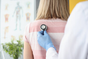 Picture of a doctor holding a stethoscope on the left side of a patient's upper back.