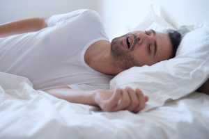 Picture of a man snoring while he is lying in bed and sleeping.
